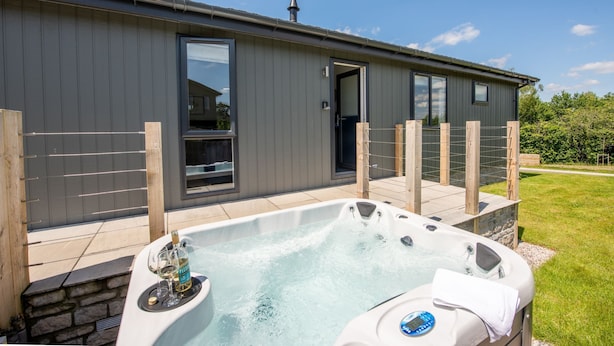 Een modern gebouw met een ruime jacuzzi ervoor, een houten omheining en een heldere lucht.