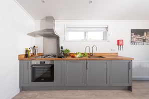 A modern kitchen with grey cabinets, a Bosch oven, a stainless steel range hood, and a wooden countertop. - Lavender Lodge, 8 Roadford Lake Lodges (Lifton)