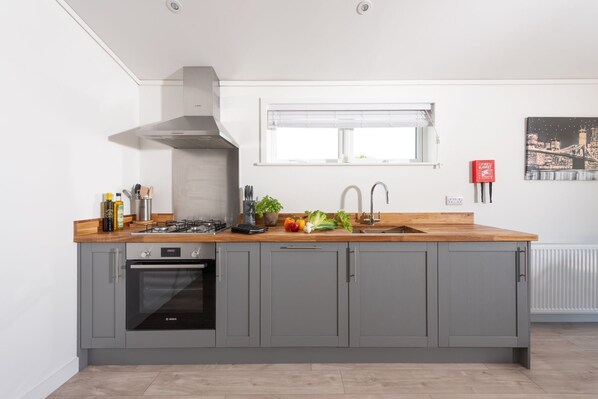 A modern kitchen with grey cabinets, a Bosch oven, a stainless steel range hood, and a wooden countertop.