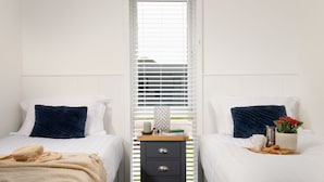 A hotel room with two beds, a small wooden nightstand, and a window with blinds.
