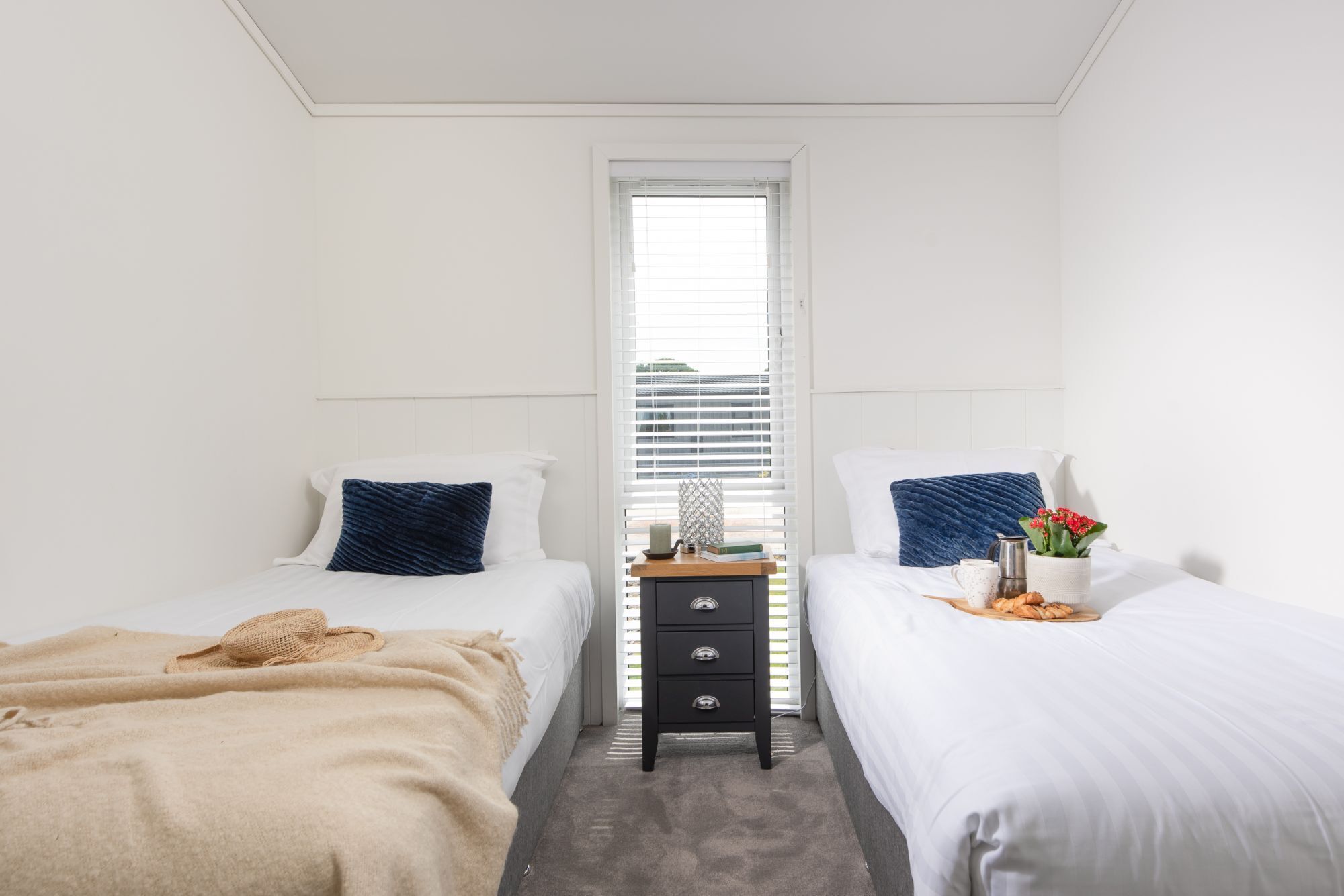 A bedroom with two beds, a nightstand, and a window with blinds.