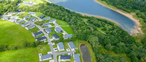 Vue aérienne d’un quartier résidentiel avec des maisons, un lac et une zone boisée.