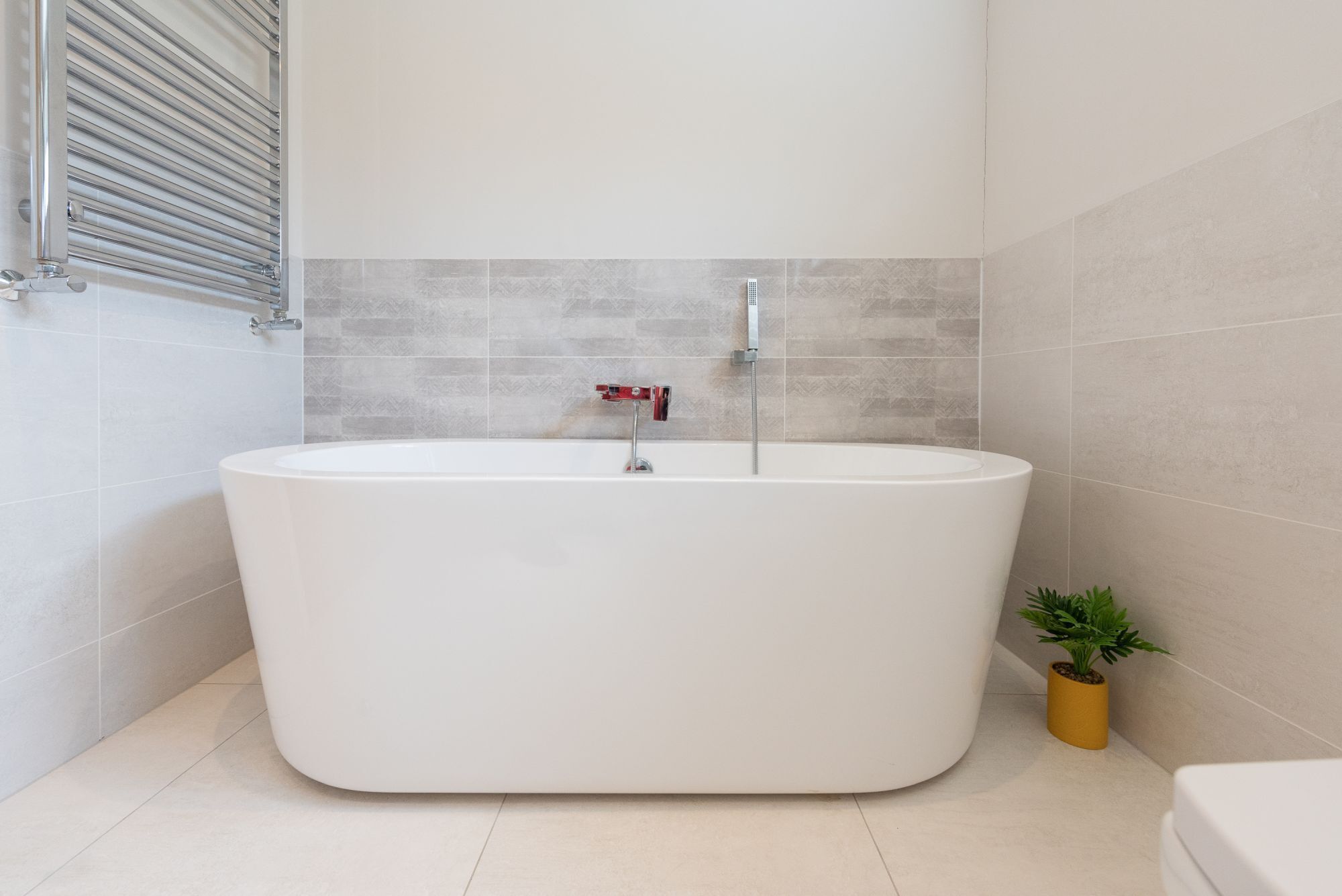 A modern bathroom with a freestanding bathtub, a showerhead, and a small potted plant.