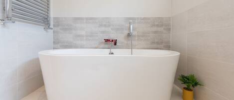 A modern bathroom with a freestanding bathtub, a showerhead, and a small potted plant.