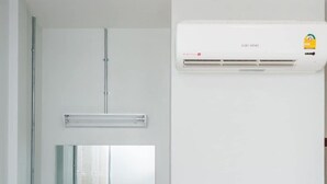 A modern bathroom with a white vanity, a red chair, a mirror, and a wall-mounted air conditioner. - Get Sleep (Tha Sala)