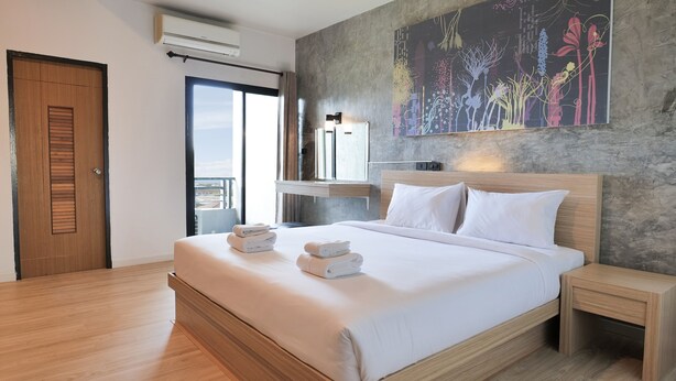 A modern hotel room with a large bed, a wooden headboard, a nightstand, and a wall-mounted air conditioner. - B2 Chiang Rai Phahonyothin Boutique & Budget Hotel (Chiang Rai)