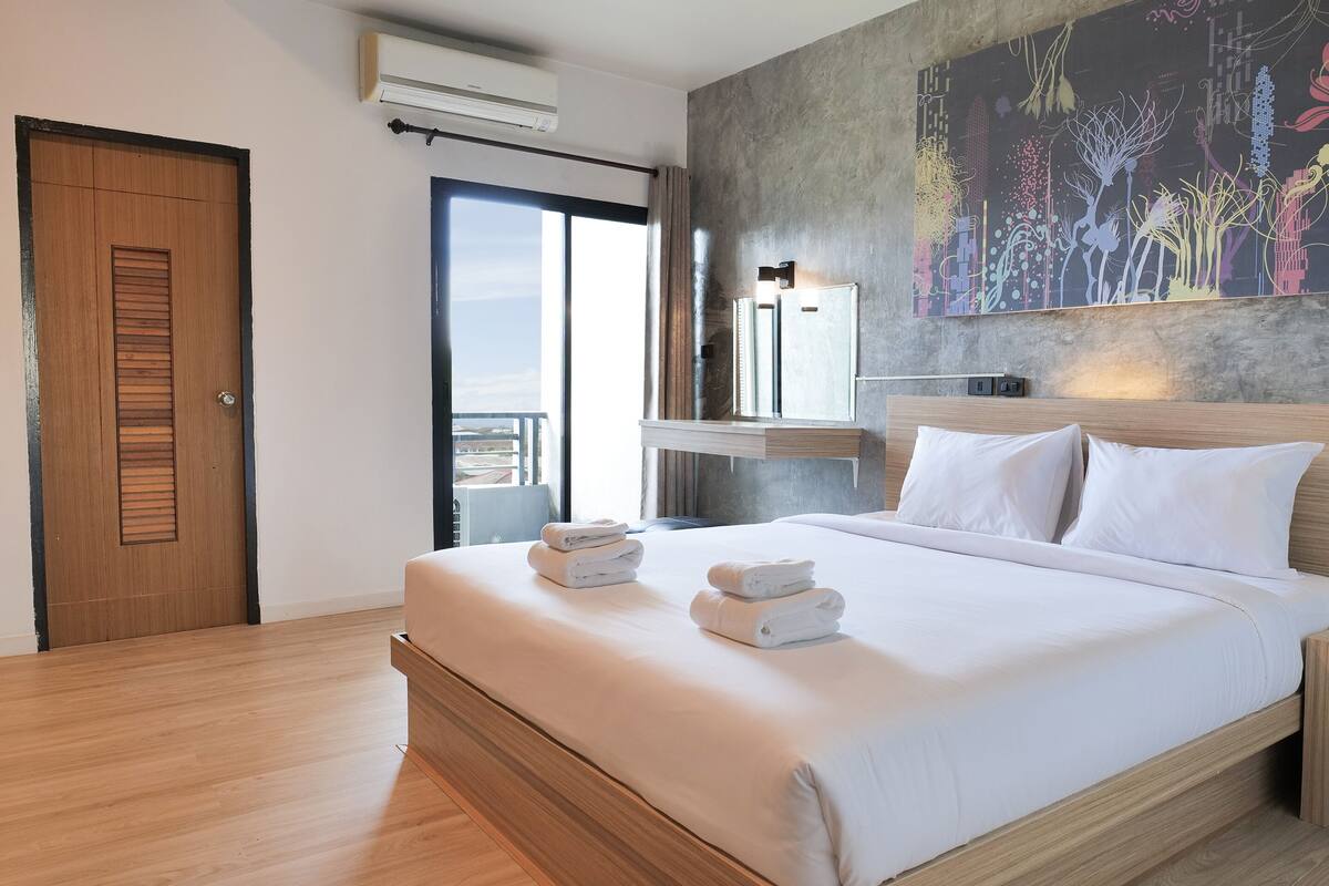 Quarto de hotel moderno com uma cama grande, cabeceira de madeira, mesa de cabeceira e ar condicionado fixado na parede.
