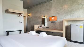 Habitación de hotel con cama, mesita de noche, espejo, televisor montado en la pared y refrigerador.