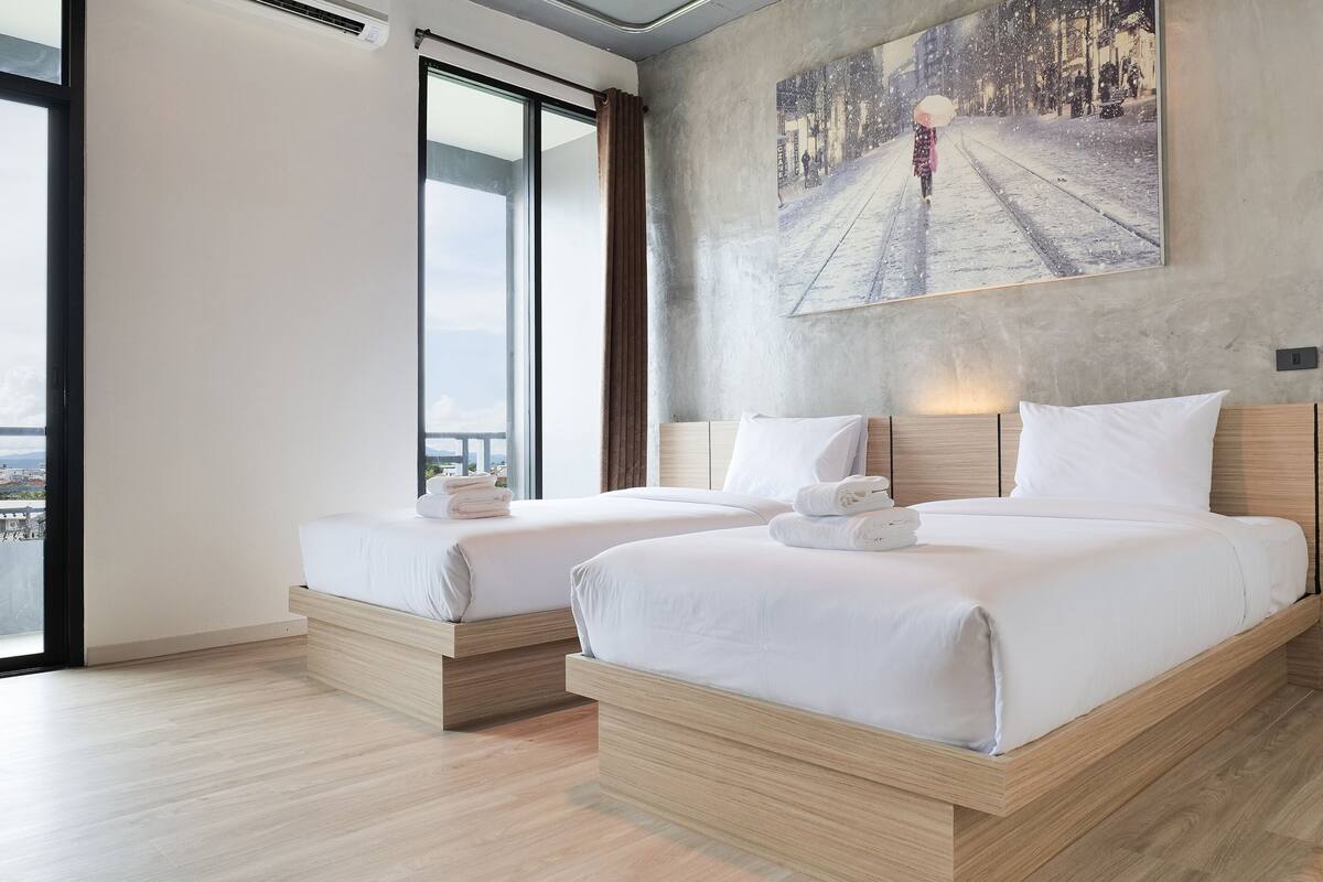 Quarto de hotel moderno com duas camas, uma janela grande e vista para a cidade.