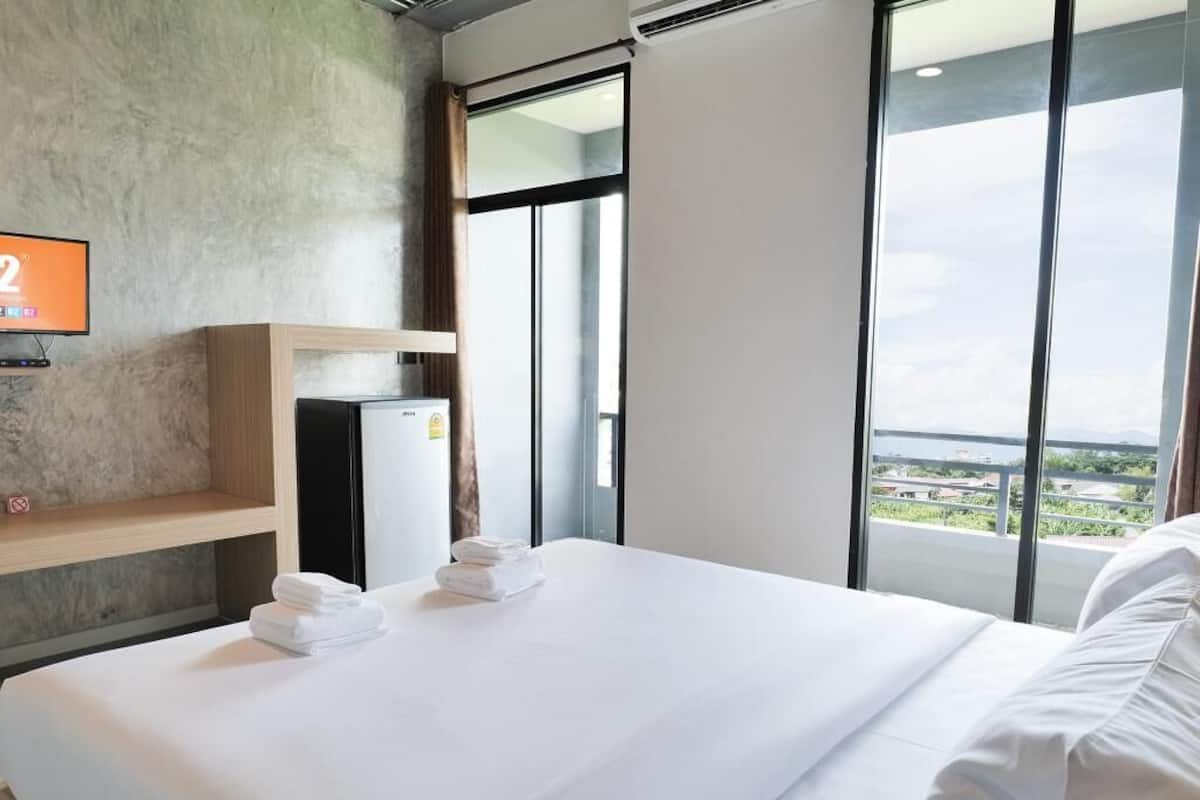 Quarto de hotel com uma cama, televisão, prateleira de madeira e vista da cidade.