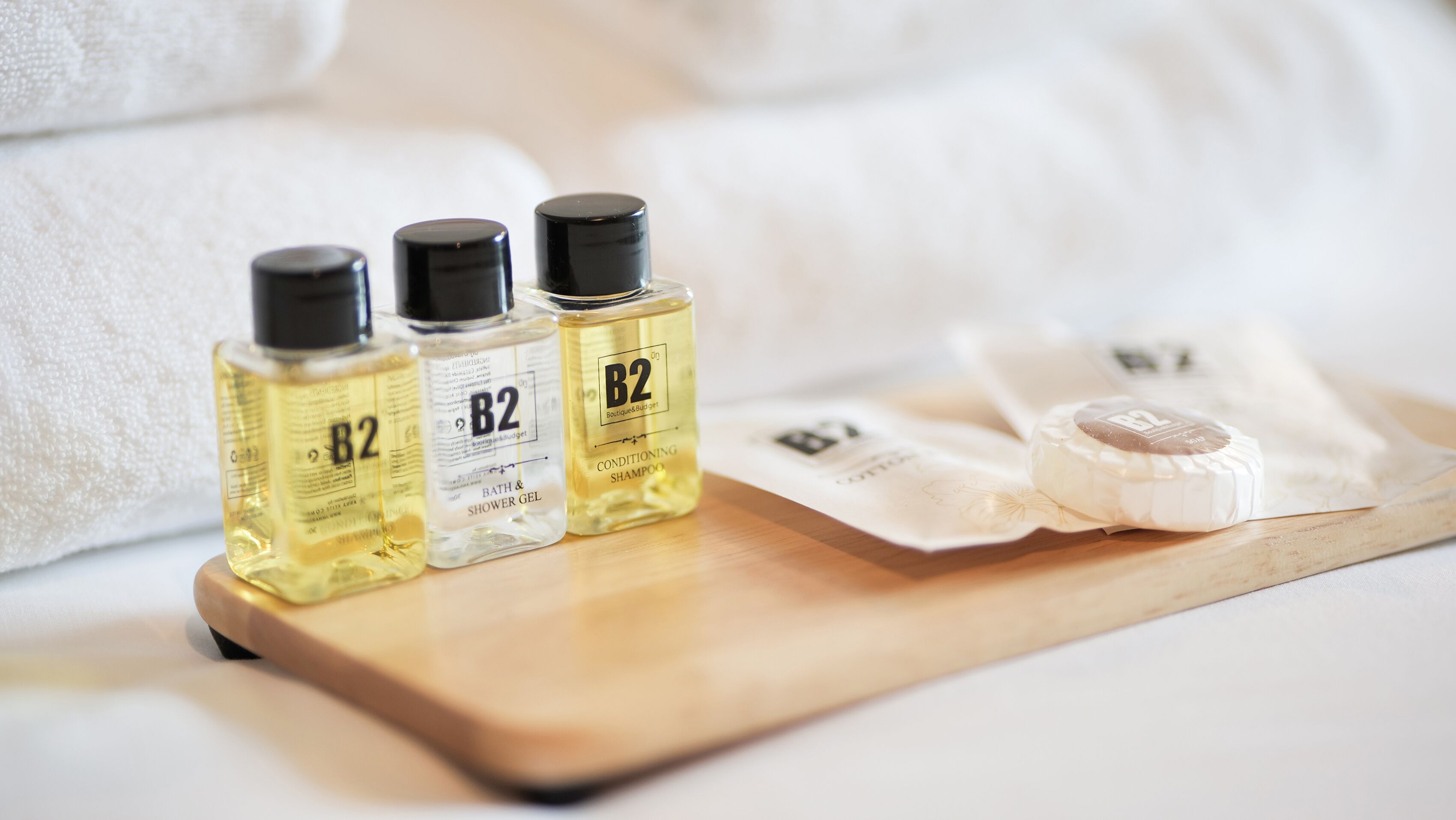 Tre flaconi di bagnoschiuma e doccia B2, una saponetta e un vassoio di legno su un letto.