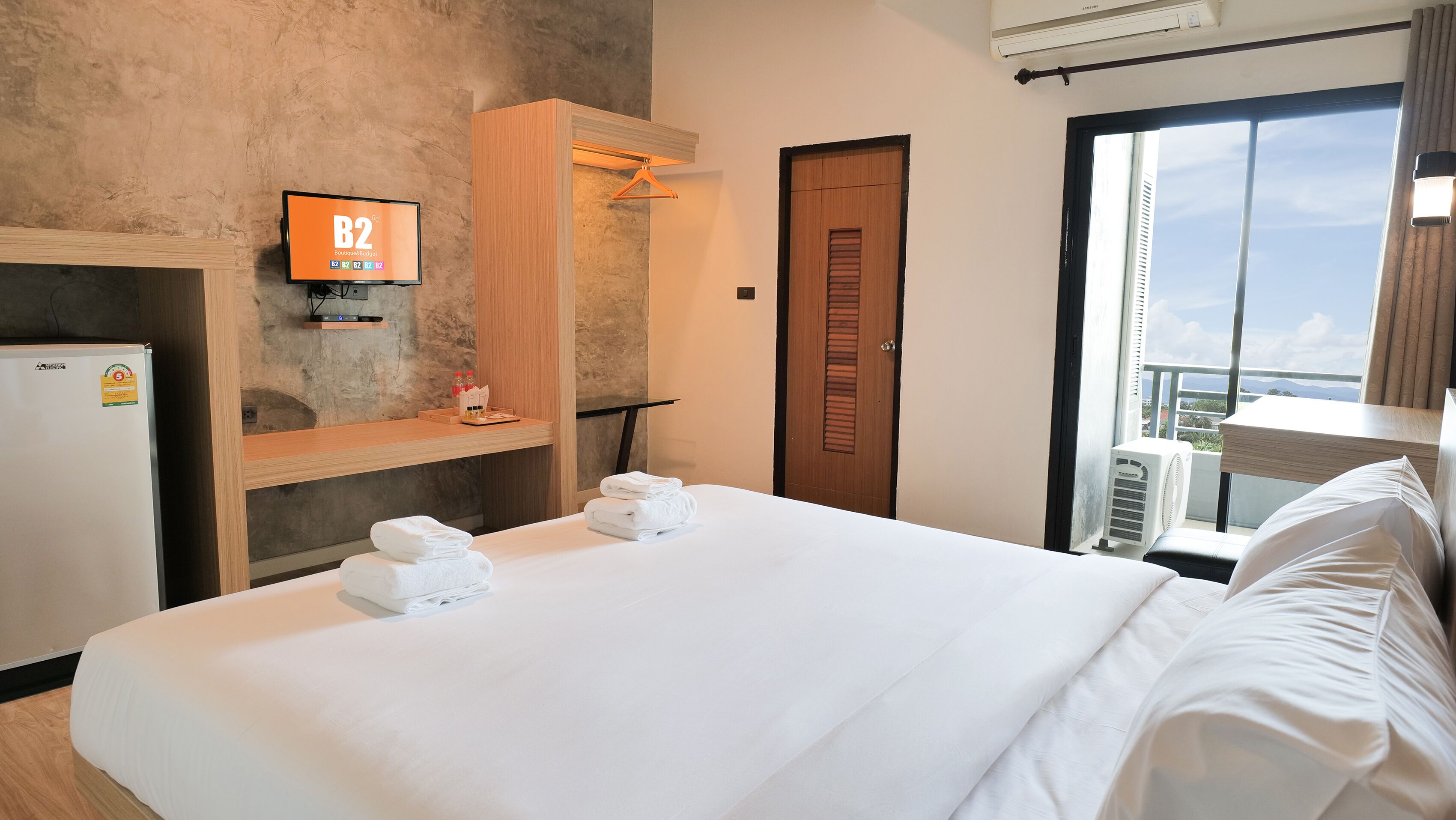 A hotel room with a bed, a TV, a minibar, and a balcony with a view.