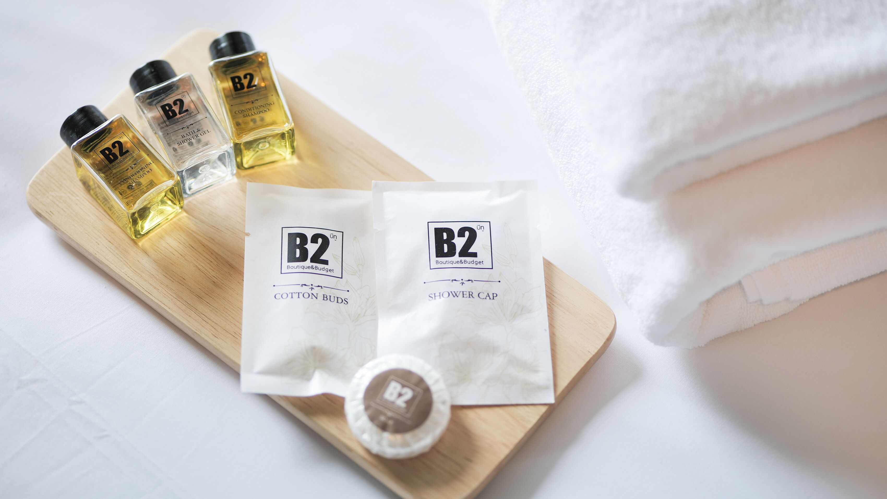 A wooden tray with three bottles of B2 conditioning shampoo, two cotton bud packets, and a shower cap.