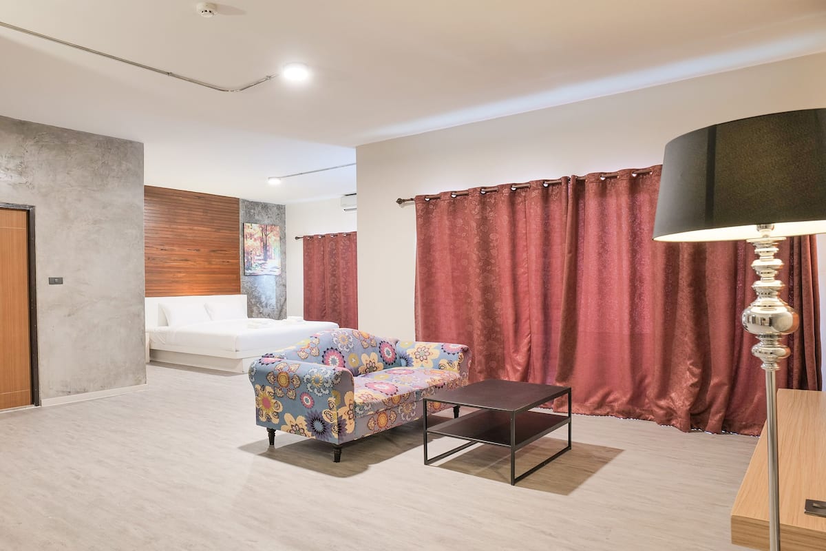 Quarto de hotel moderno com uma cama, um sofá colorido, uma mesinha e uma luminária.