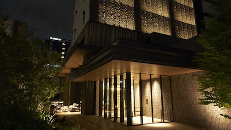 A modern building with a glass facade, outdoor seating area, and a visible sign for a nearby hotel.