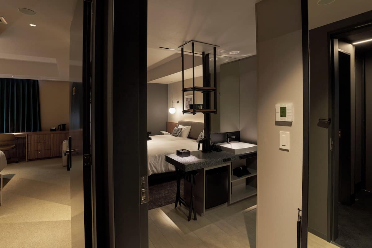 A modern hotel room with a bed, bedside table, and a small kitchenette.
