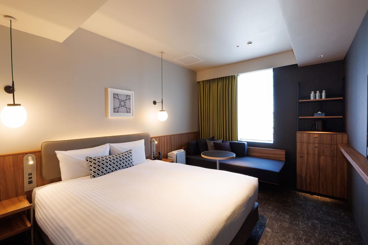 A hotel room with a large bed, a small sofa, a desk, and a cabinet.