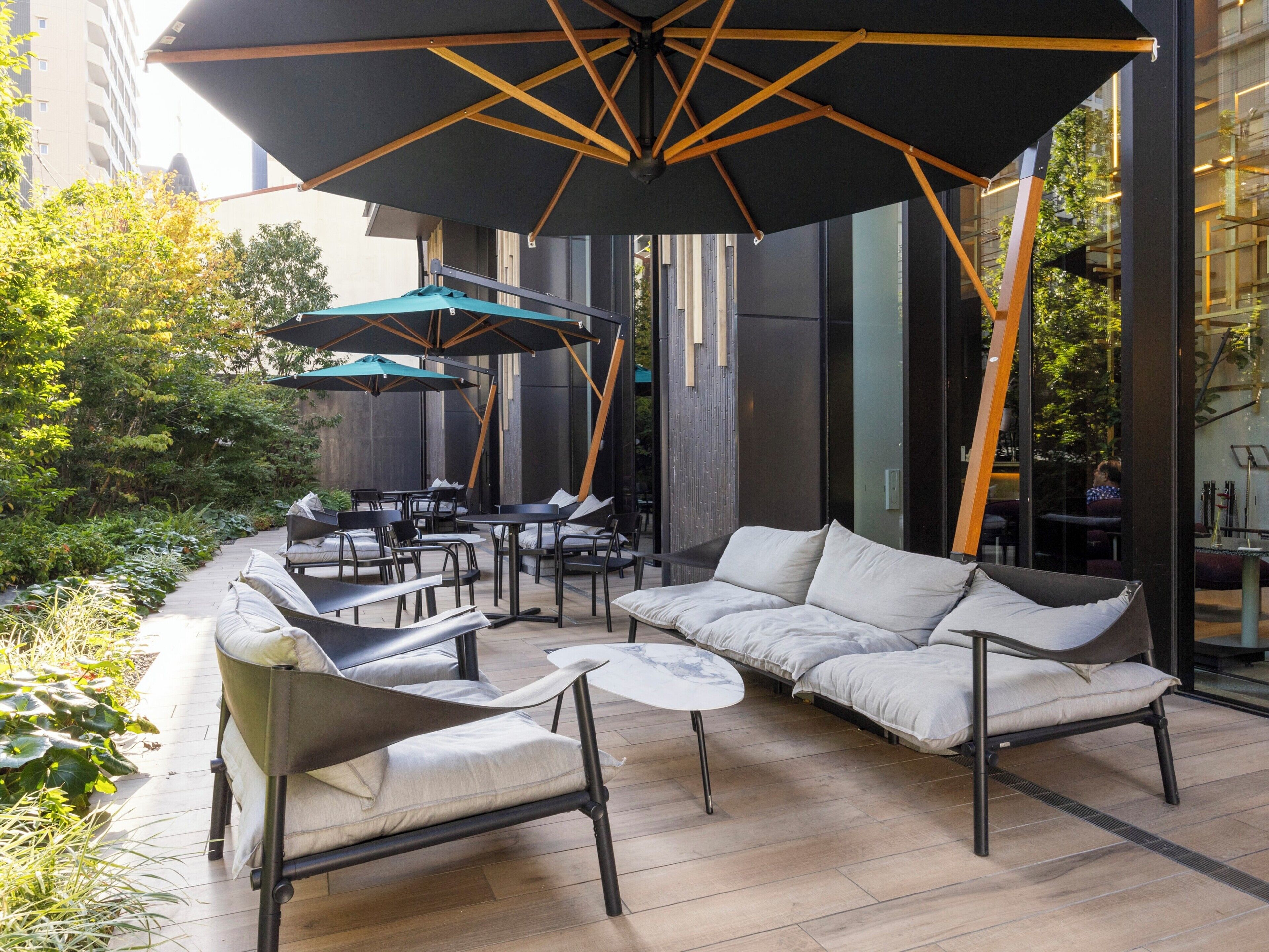 Ein Außenbereich mit modernen Möbeln, darunter eine Couch und Stühle, beschattet durch große Sonnenschirme.