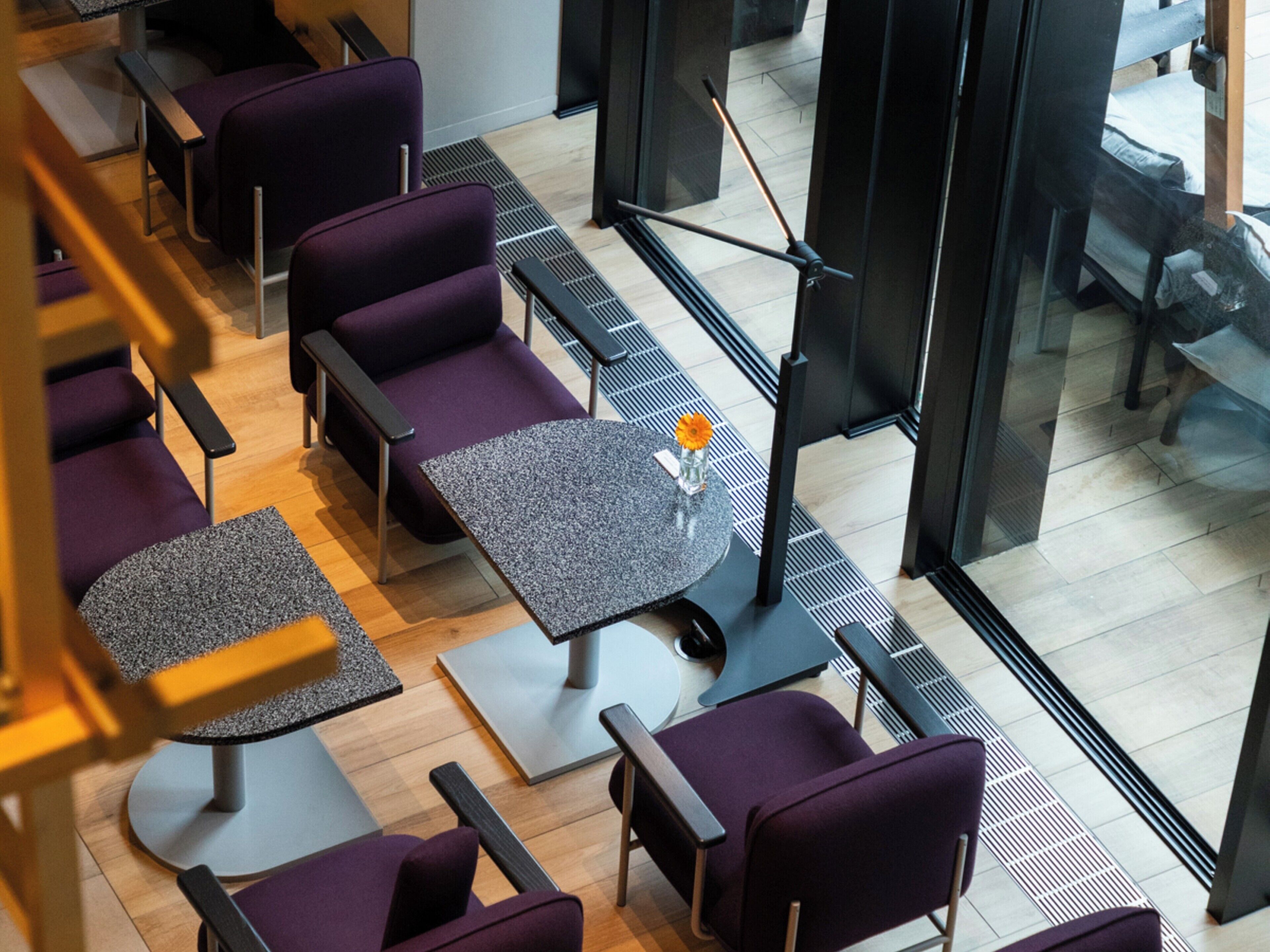A modern interior with purple seating, a round table with a vase, and a view through large windows.
