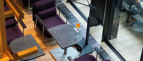 A modern interior with purple seating, a round table with a vase, and a view through large windows.