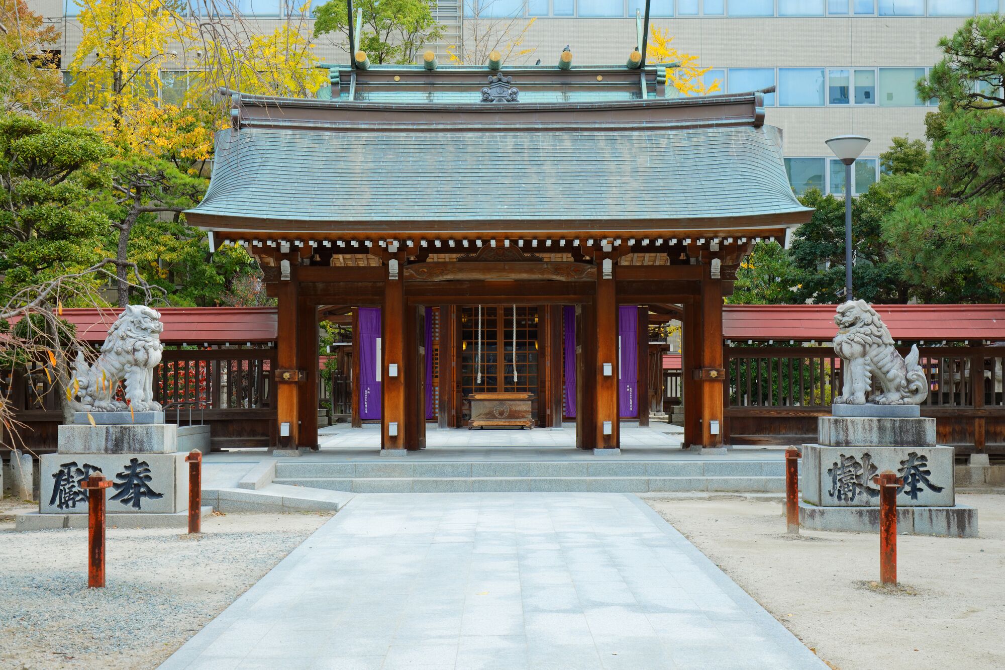 Un bâtiment traditionnel japonais, avec un toit recouvert de tuiles, des piliers en bois et deux statues de lions à l’entrée.