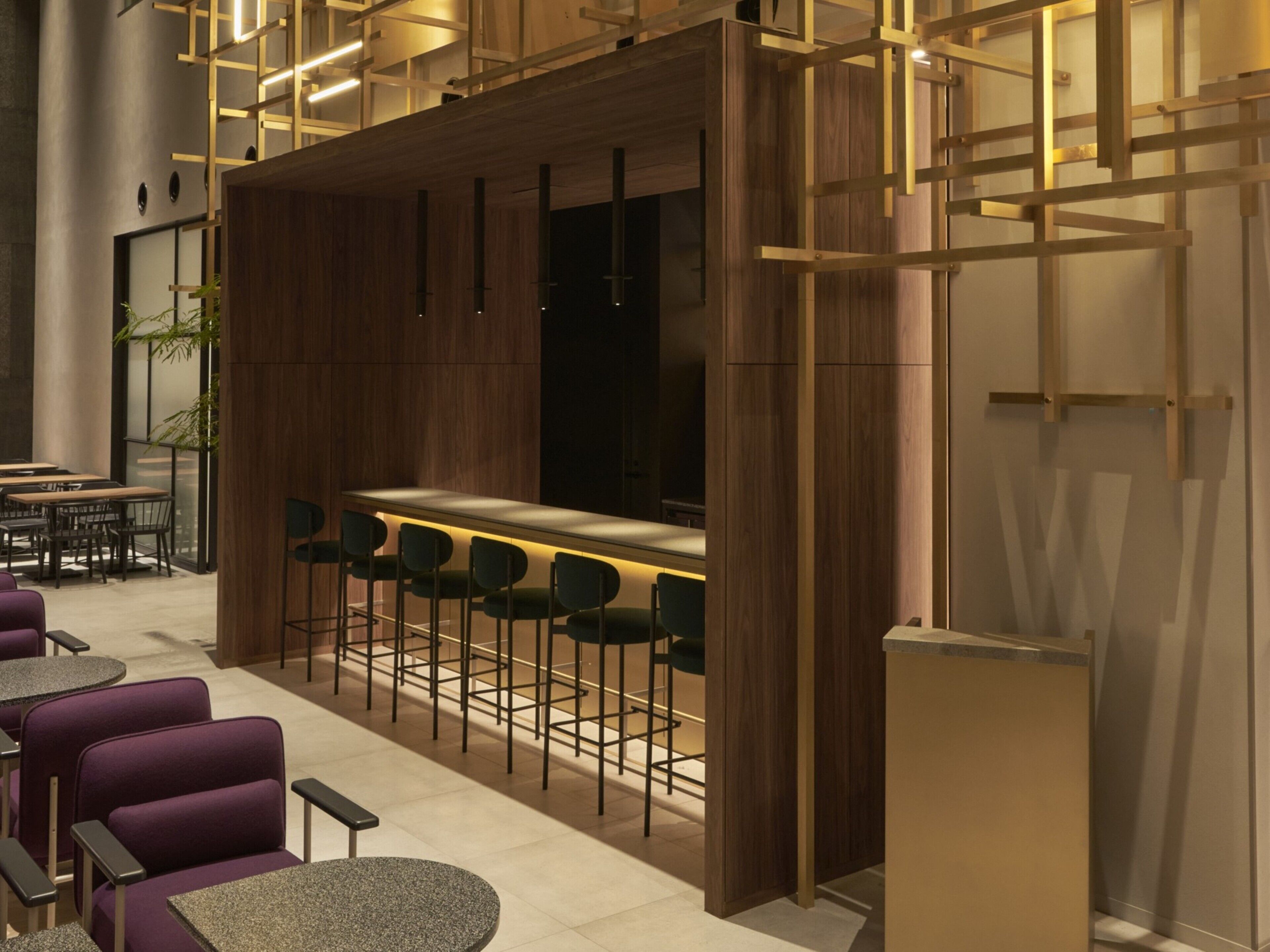Un área de bar moderna con paneles de madera, taburetes y un espacio de estar con mesas redondas y sillas.