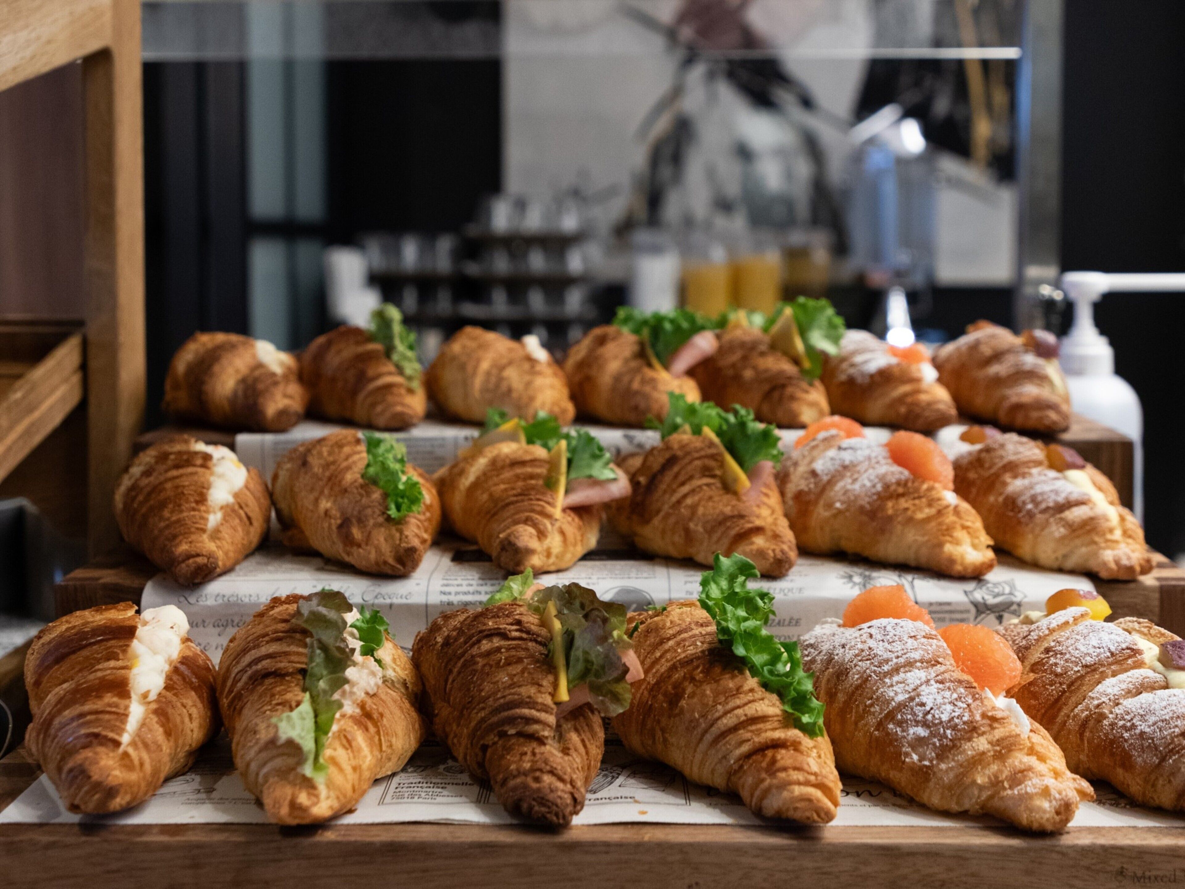 A display of assorted pastries, including croissants and sandwiches, arranged on a wooden surface.