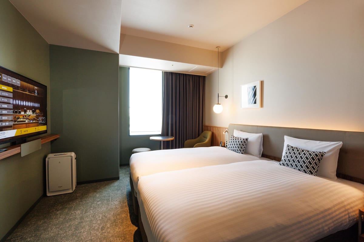 A hotel room with a large bed, a desk, a chair, a TV, and a window with curtains.