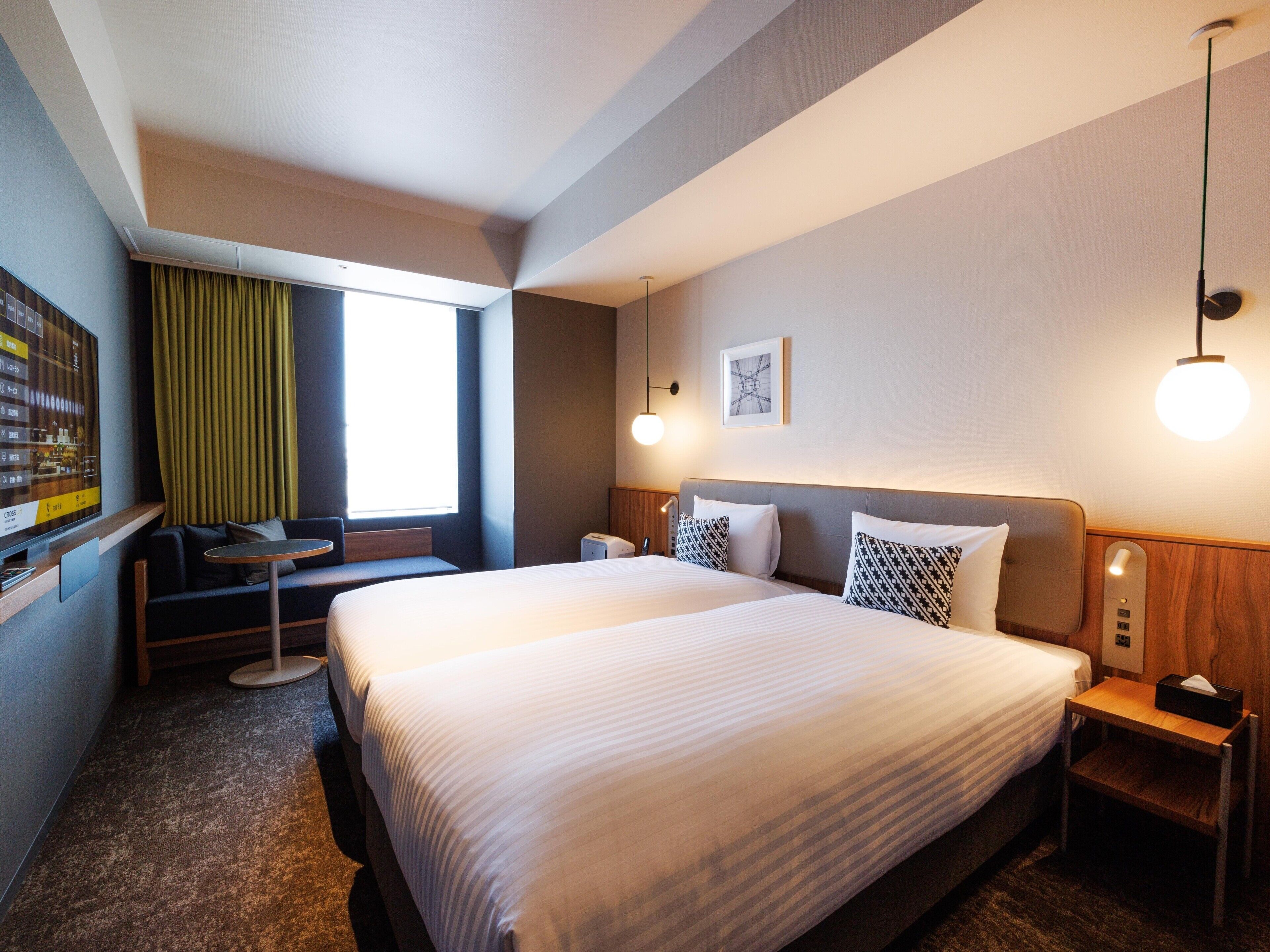 A hotel room with a large bed, a small seating area, a desk, and a window with curtains.