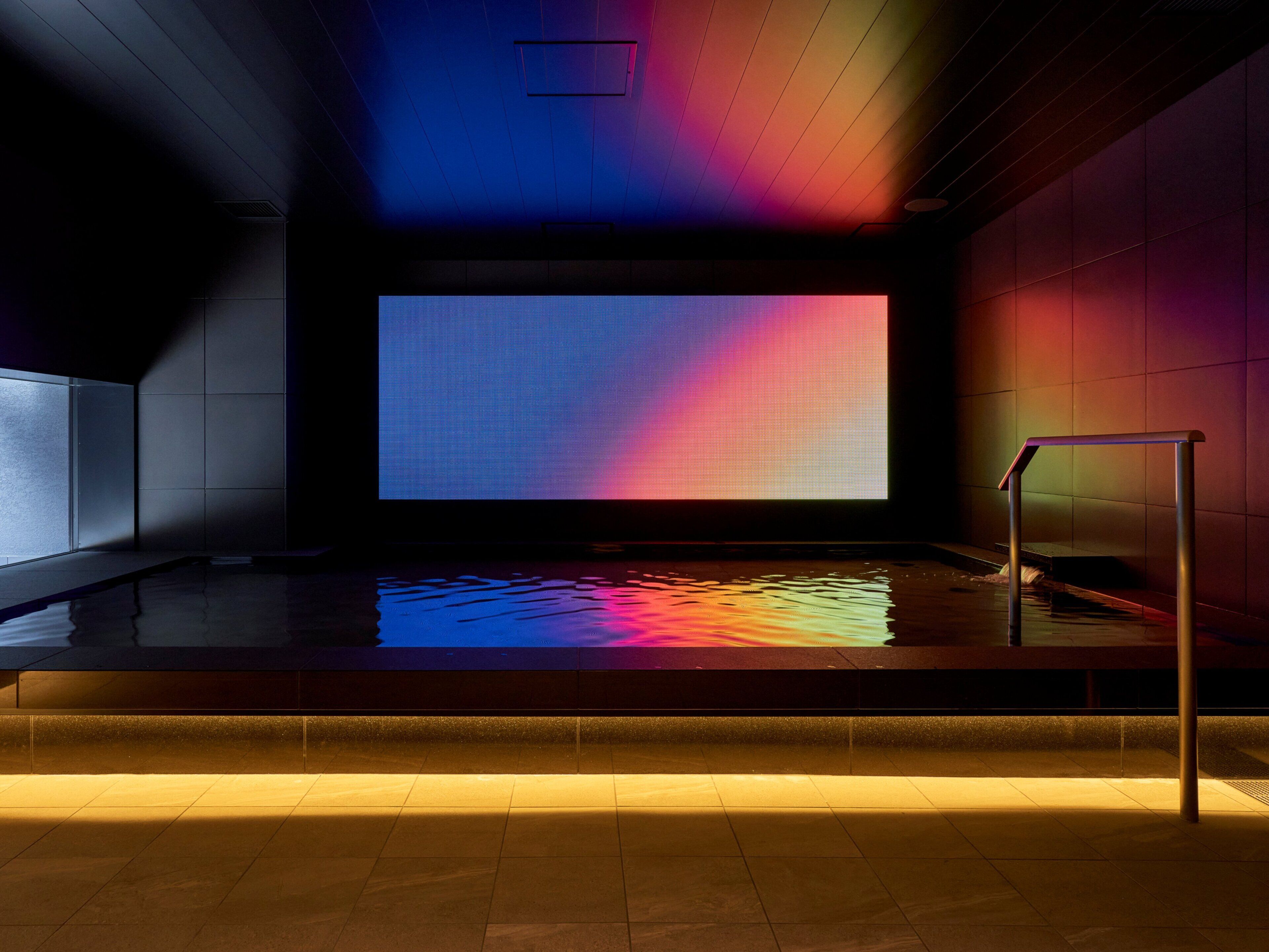 A modern indoor pool area with a large digital screen displaying a colorful gradient.