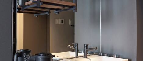 A modern bathroom with a large mirror, two sinks, a coffee machine, and a trash bin.