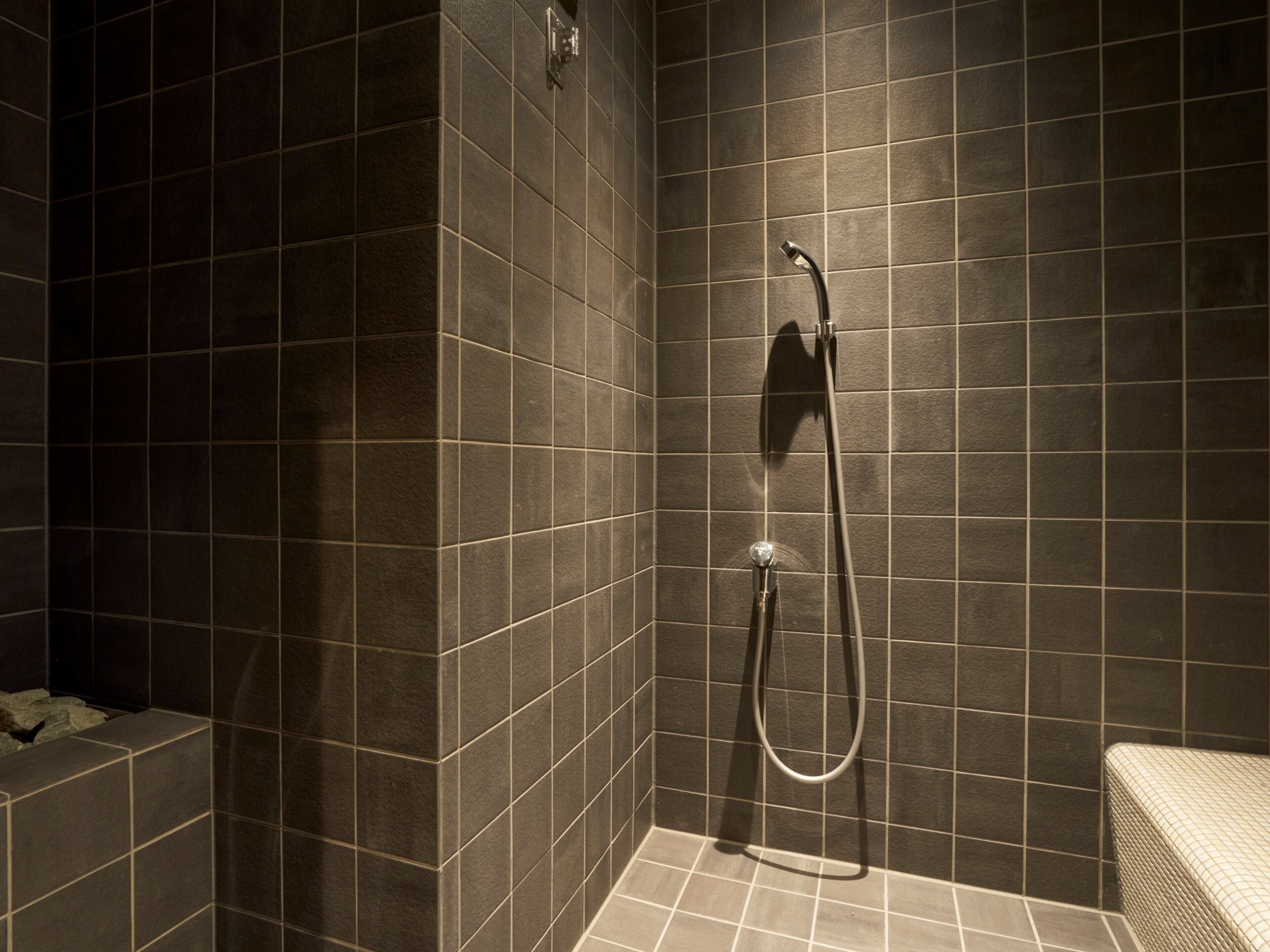 A modern shower with dark tiles and a handheld showerhead.