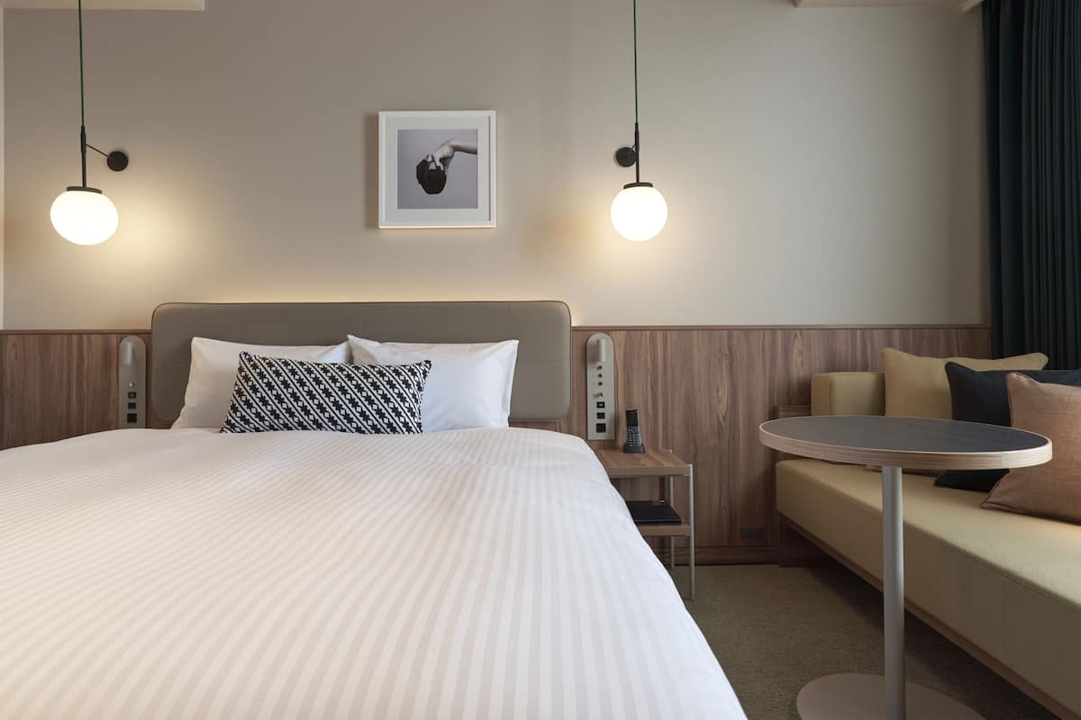 A hotel room with a large bed, a bedside table, a round table, a sofa, and two pendant lights.