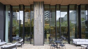 A modern indoor space with large glass windows, a central wooden column, and seating areas with tables and chairs. - Cross Life Hakata Tenjin （ORIX HOTELS & RESORTS） (Fukuoka)