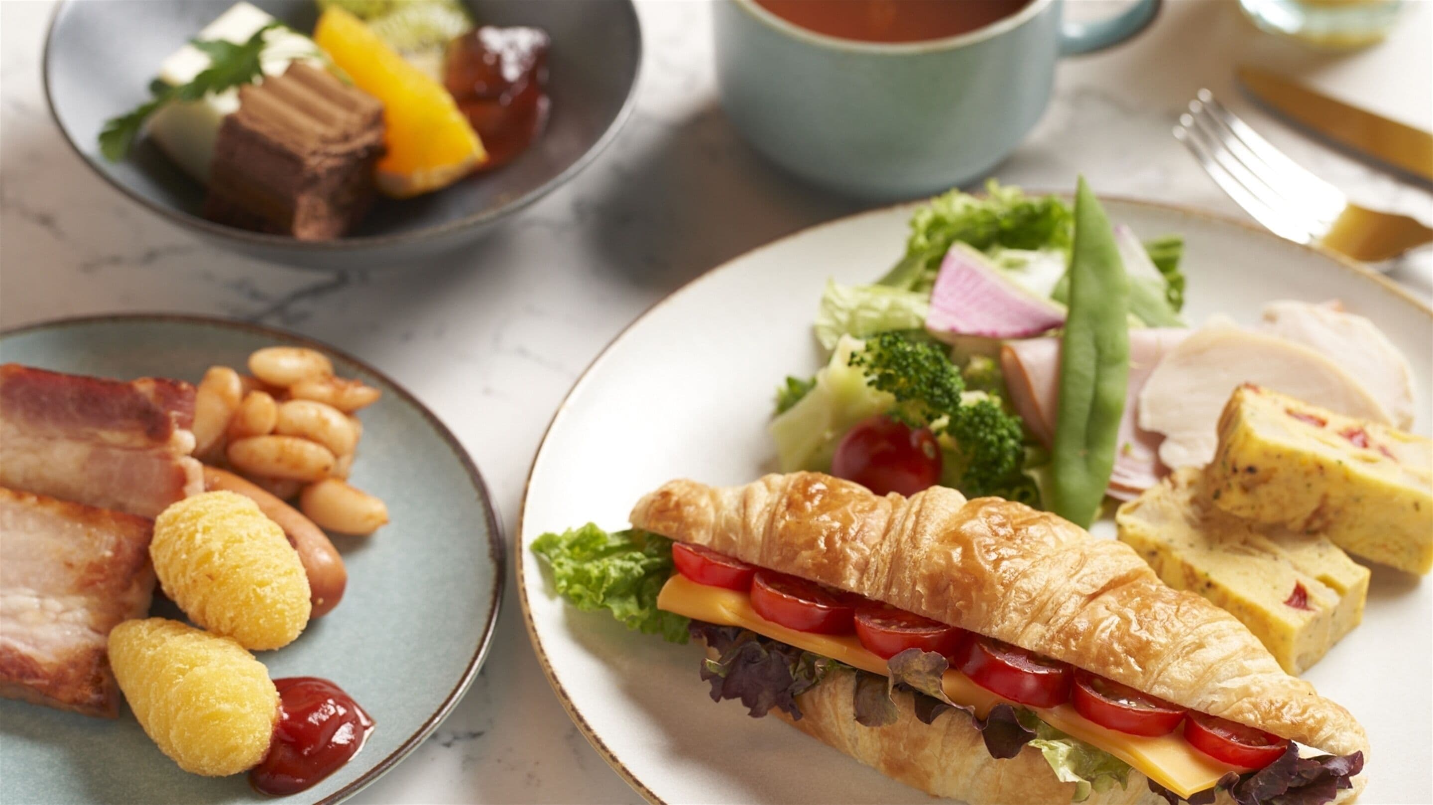 Una mesa con platos de comida, incluyendo un sándwich de croissant, frijoles y carne.