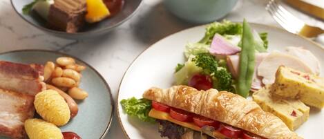 Una mesa con platos de comida, incluyendo un sándwich de croissant, frijoles y carne.