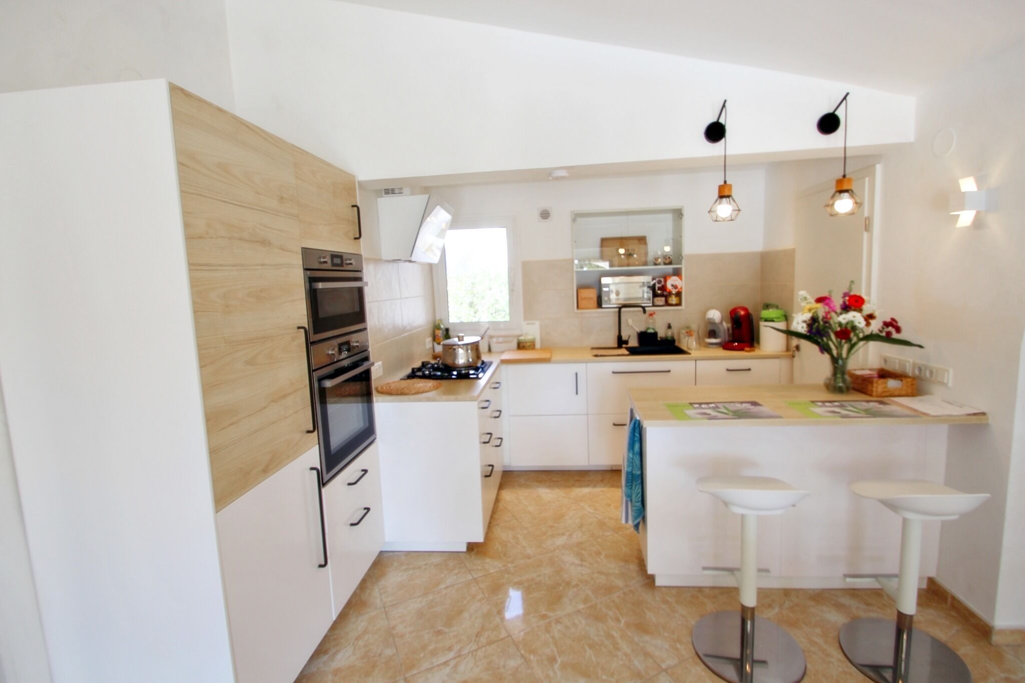 A modern kitchen with white cabinetry, a built-in oven, a gas stove, and a small island with bar stools.