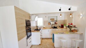 A modern kitchen with white cabinetry, a built-in oven, a gas stove, and a small island with bar stools. - La Tranquilidad - private pool villa with panoramic views in Moraira (Teluda)