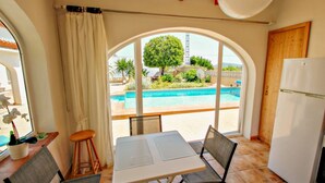 A room with a large arched window, a dining table with chairs, a refrigerator, and a potted orchid. - La Tranquilidad - private pool villa with panoramic views in Moraira (Teluda)
