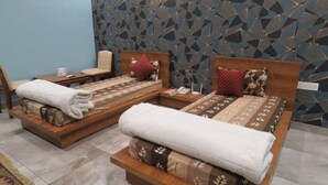 Deux lits en bois avec une literie à motifs floraux, une chaise, une petite table et un téléphone.