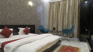 Une chambre d’hôtel avec un grand lit, deux chaises bleues, une petite table et un rideau.