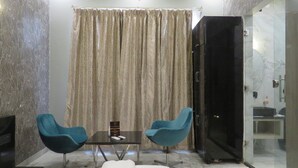 Une pièce dotée d’une porte vitrée donnant sur une salle de bain, de deux chaises bleues, d’une petite table avec une télécommande et d’un rideau à motifs ondulés.