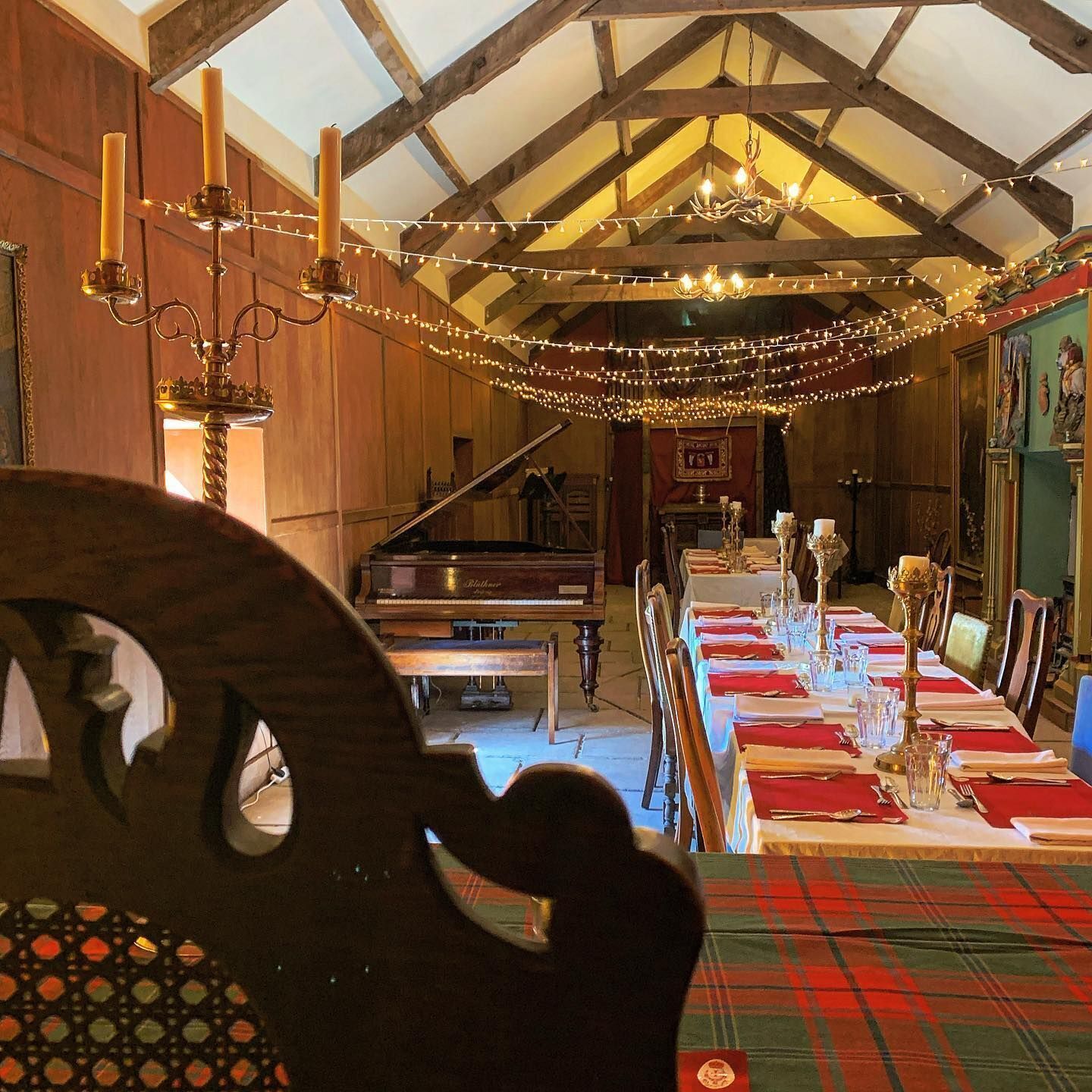 A dining area with a long table set for a meal, a grand piano, and a staircase leading to an upper level.