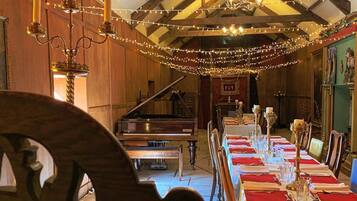 A dining area with a long table set for a meal, a grand piano, and a staircase leading to an upper level.