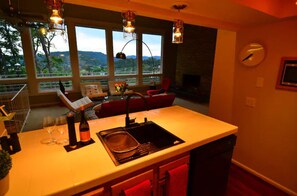 A kitchen with a large island, a sink, and a view of the outdoors. There are chairs and a table in the living area. - Amazing Mid-Century Modern Home-Incredible Views! (roseburg)
