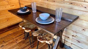 A wooden dining table with two stools, a bowl, and stacked glasses. - Table Rock Lake Tiny House Container Home Get Away (Shell Knob)