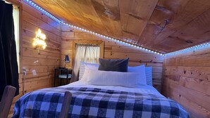 A cozy wooden cabin bedroom with a checkered bedspread, a bedside lamp, and a neon sign. - Table Rock Lake Tiny House Container Home Get Away (Shell Knob)