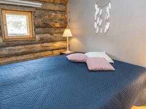 A log cabin room with a bed, a window, a lamp, and a dreamcatcher on the wall.