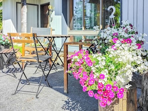 An outdoor seating area with wooden chairs and tables, a flower arrangement, and a building with a number '2' sign. - Rukaköngäs 21 by Interhome (Kuusamo)