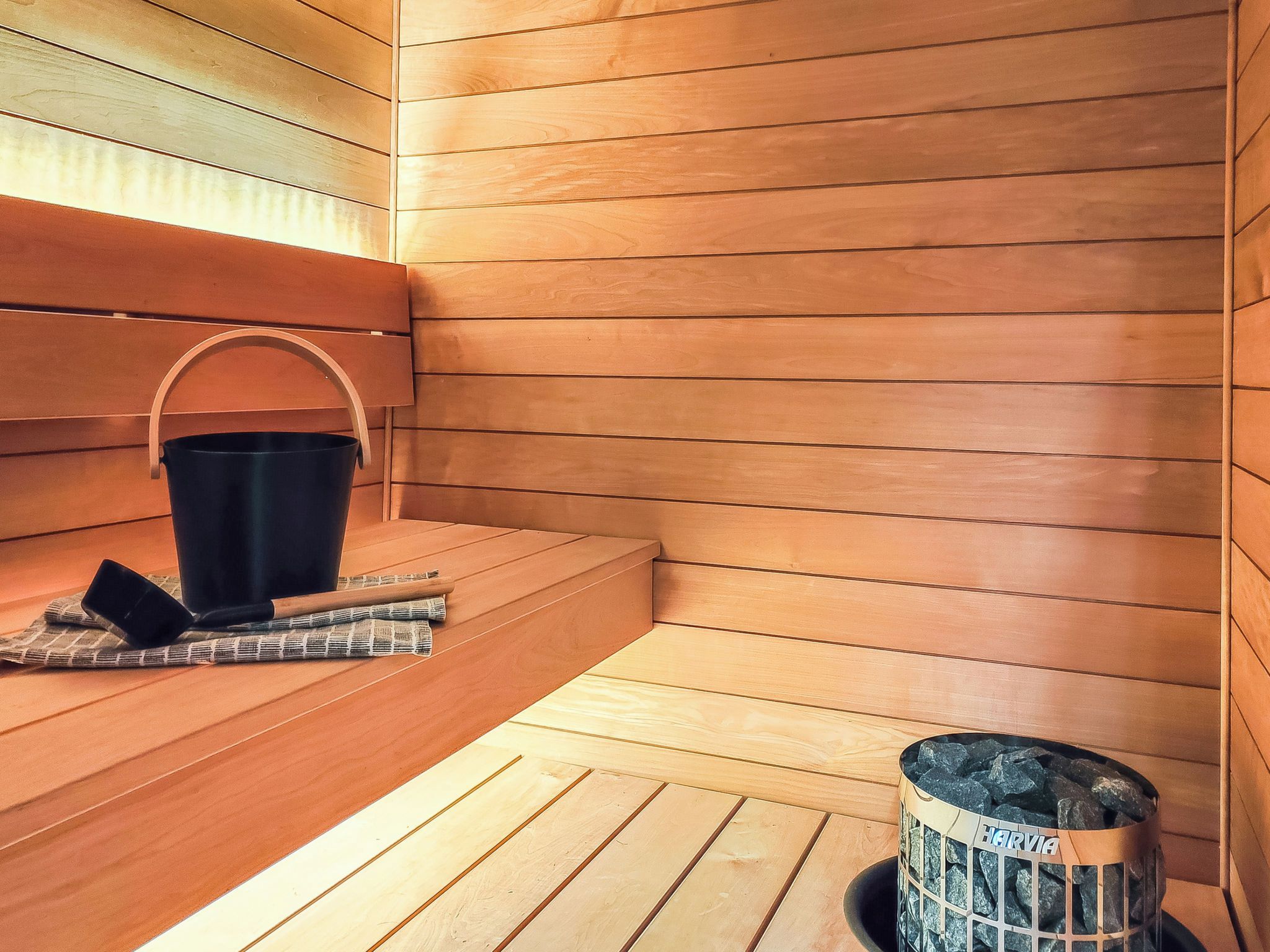 A sauna room with wooden benches, a black bucket, and a charcoal container.